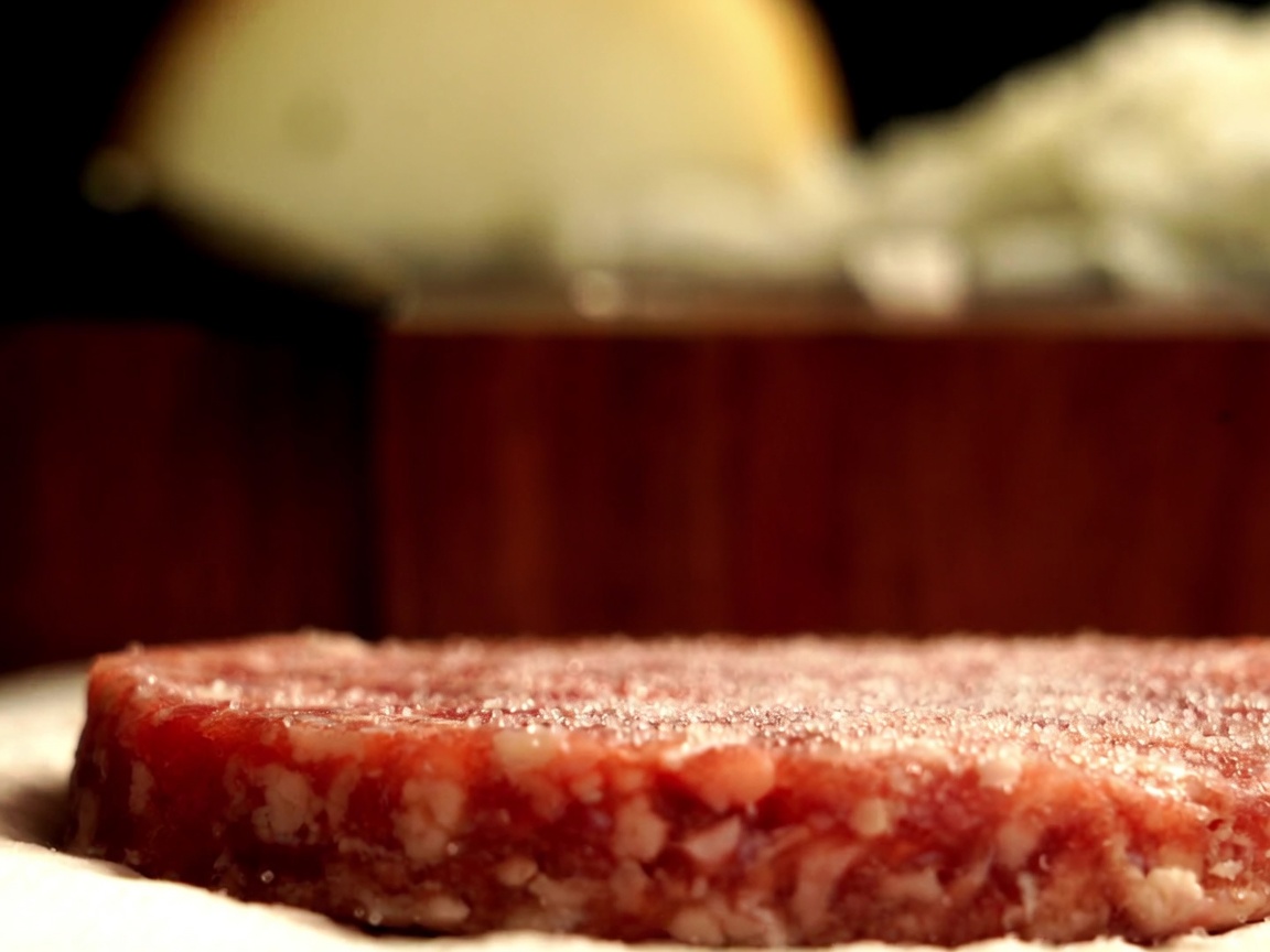 Close-up of an Australian Wagyu beef patty being seasoned with fresh black pepper from a mill.