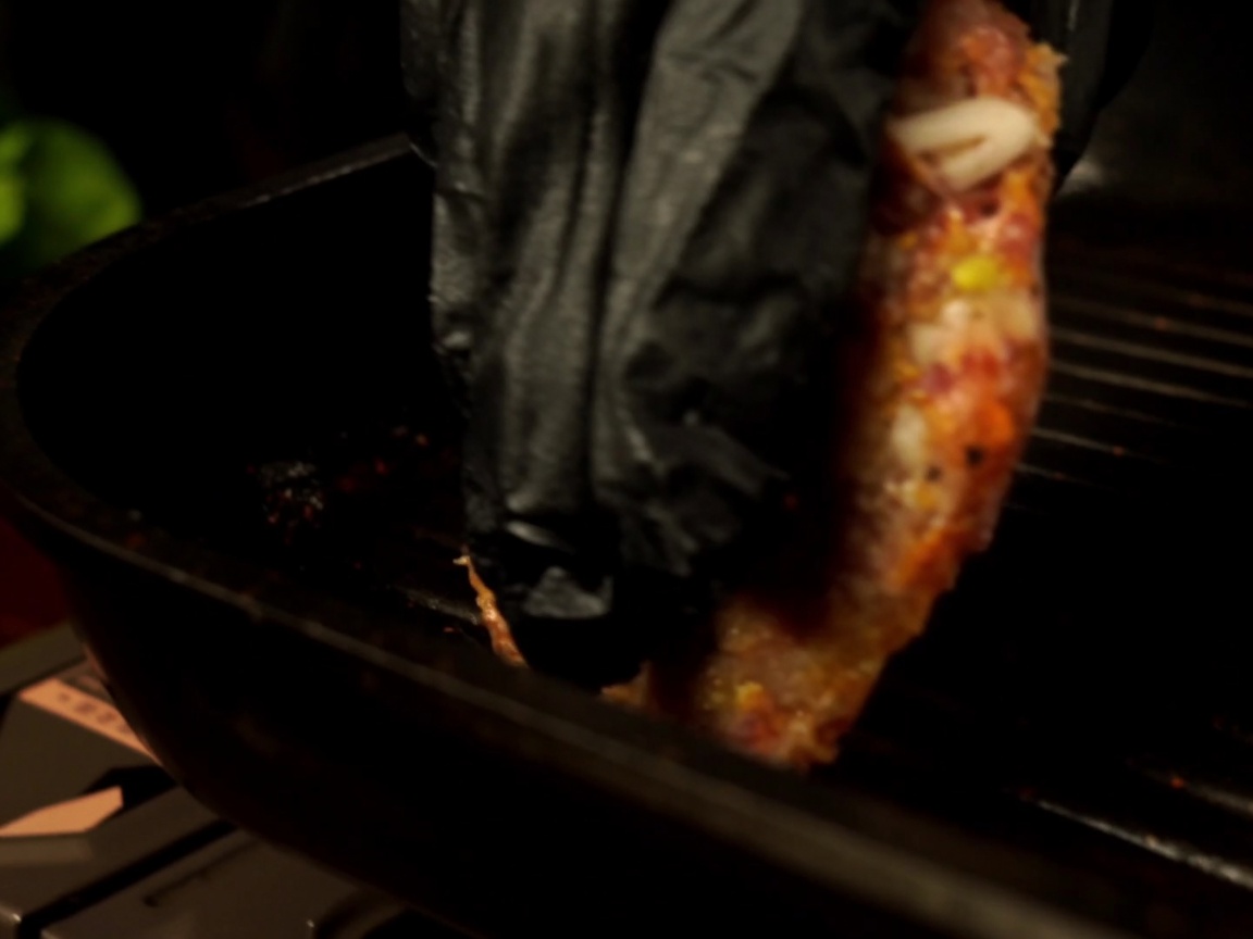 A raw beef patty being placed into a preheated grill pan.