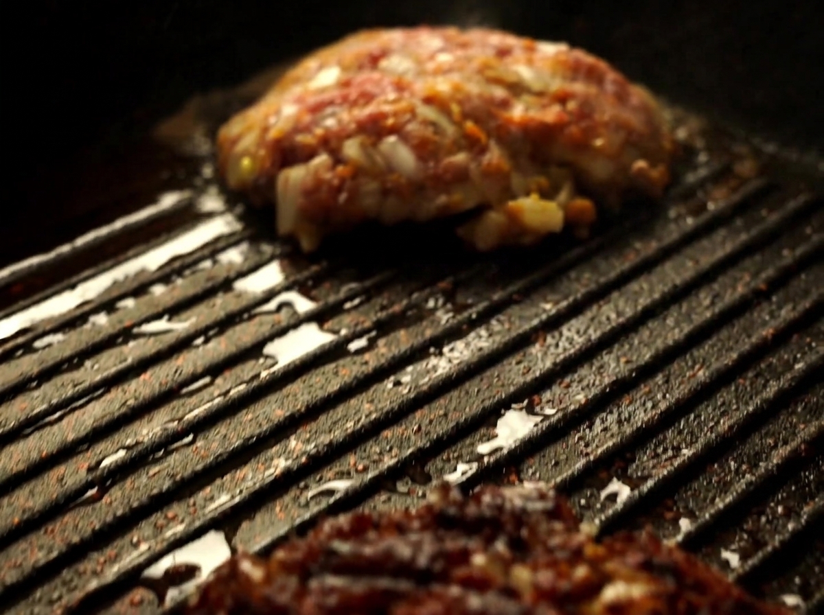 A close-up view of a Wagyu beef patty being flipped with a spatula in a hot grill pan.