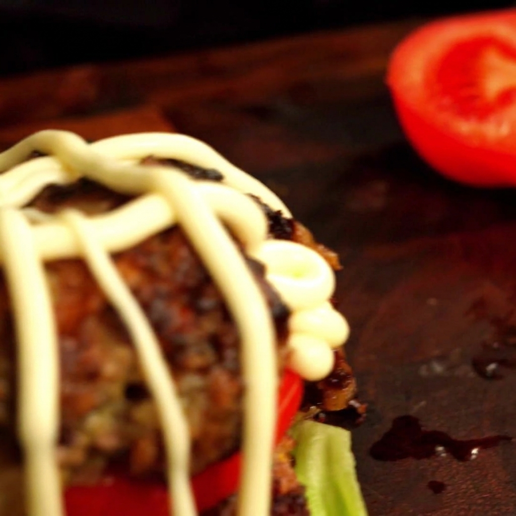 Creamy mayonnaise being drizzled in a decorative pattern over the assembled burger.