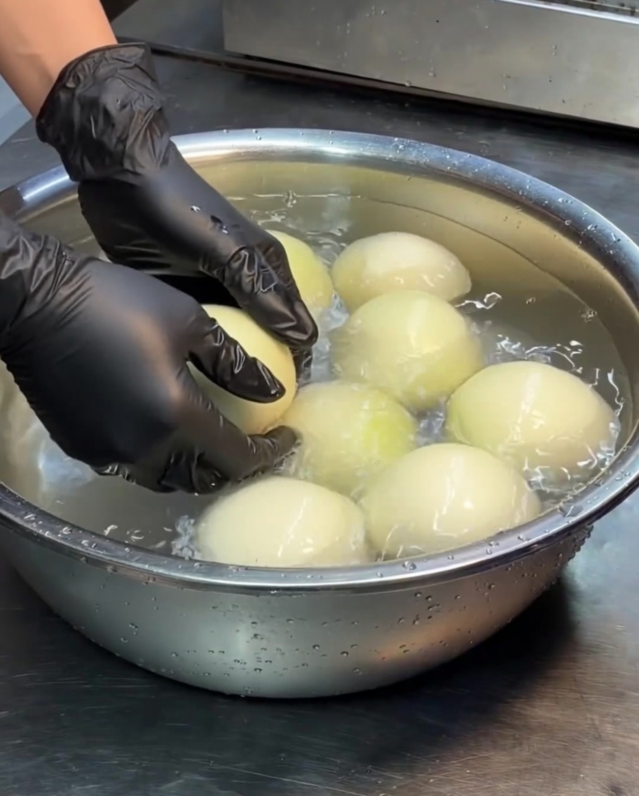 Whole white onions soaking in a stainless steel basin filled with water.