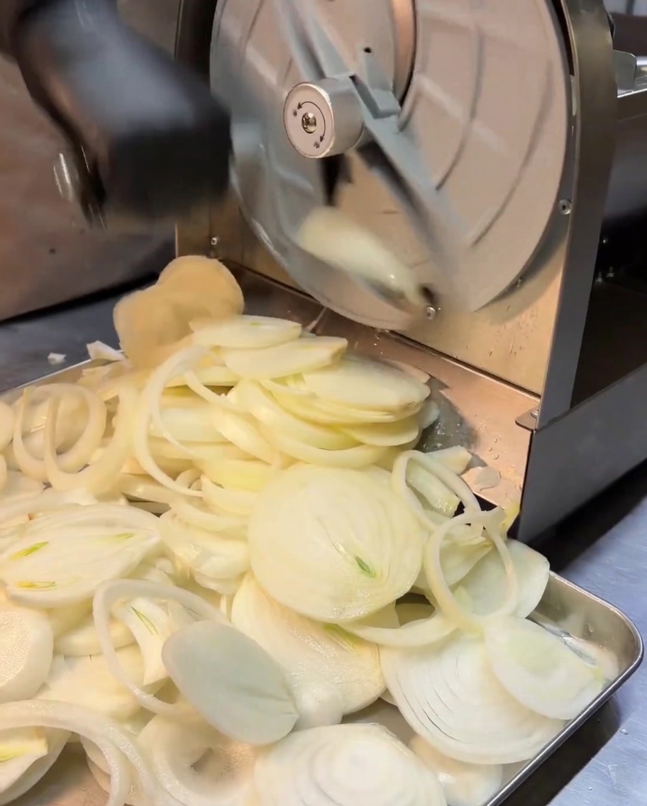 Thin shreds of white onion being processed through a rotary slicer.
