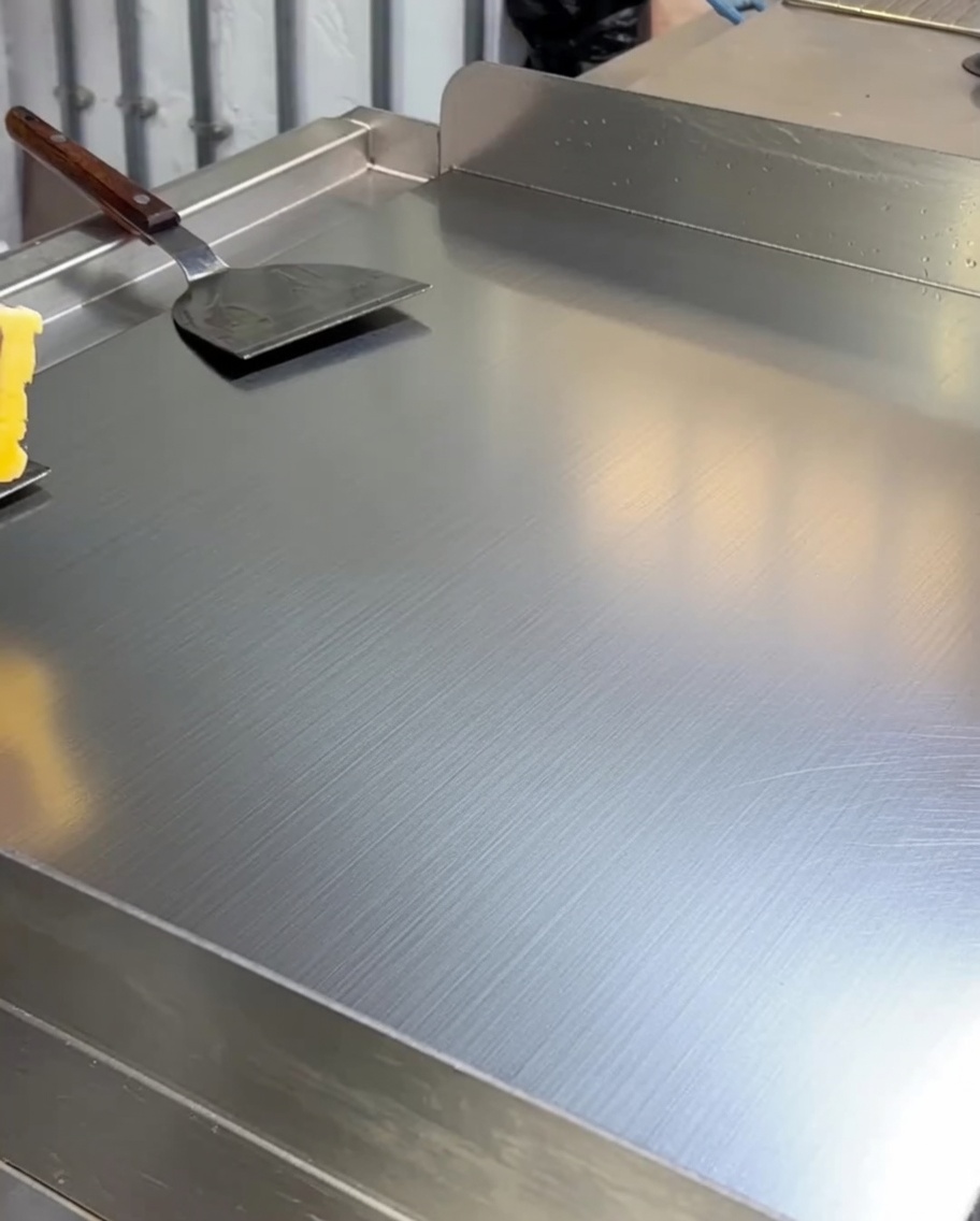 Yellow butter melting and coating the surface of a hot stainless steel griddle.