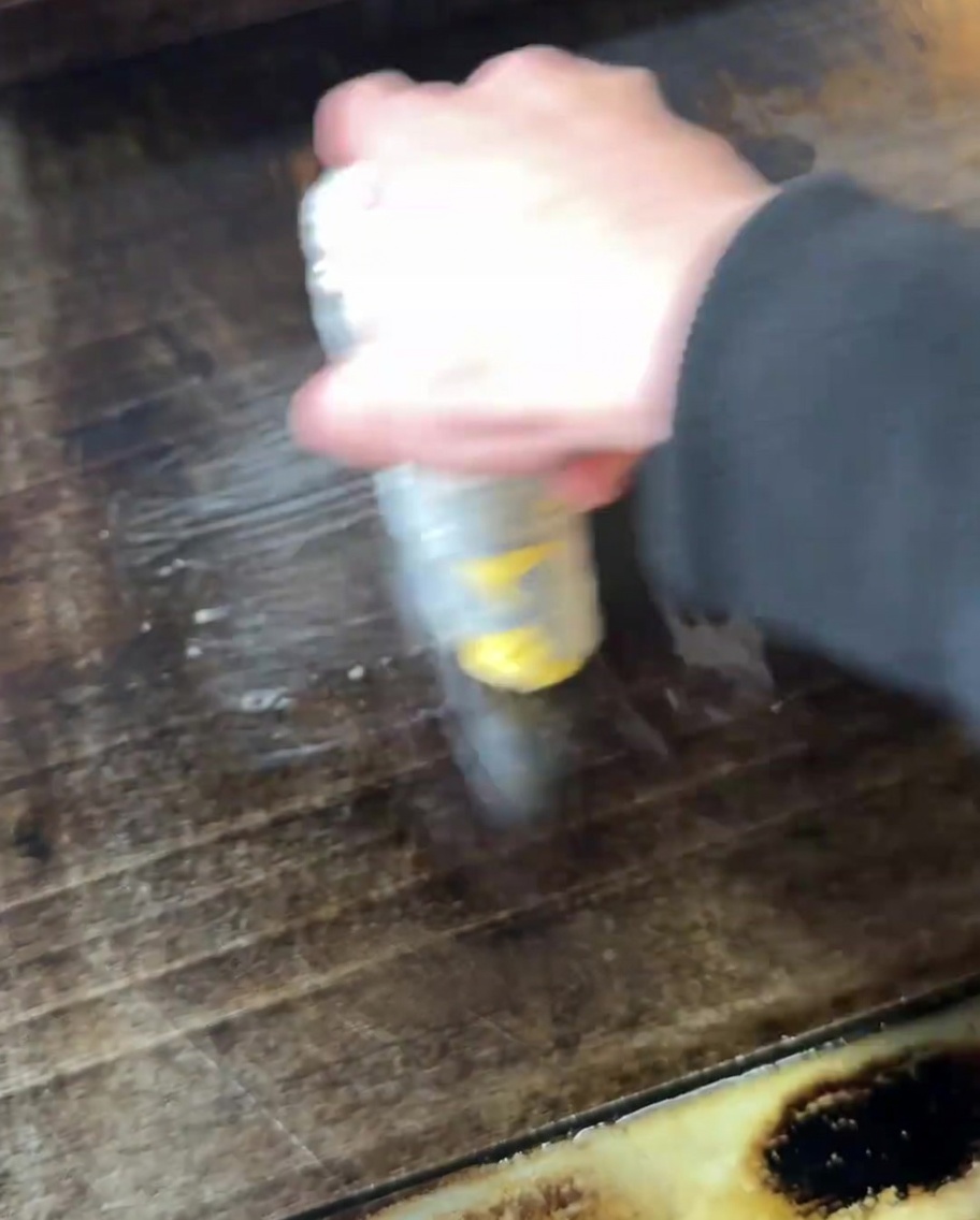 A hand brushing melted butter across the surface of a hot griddle.