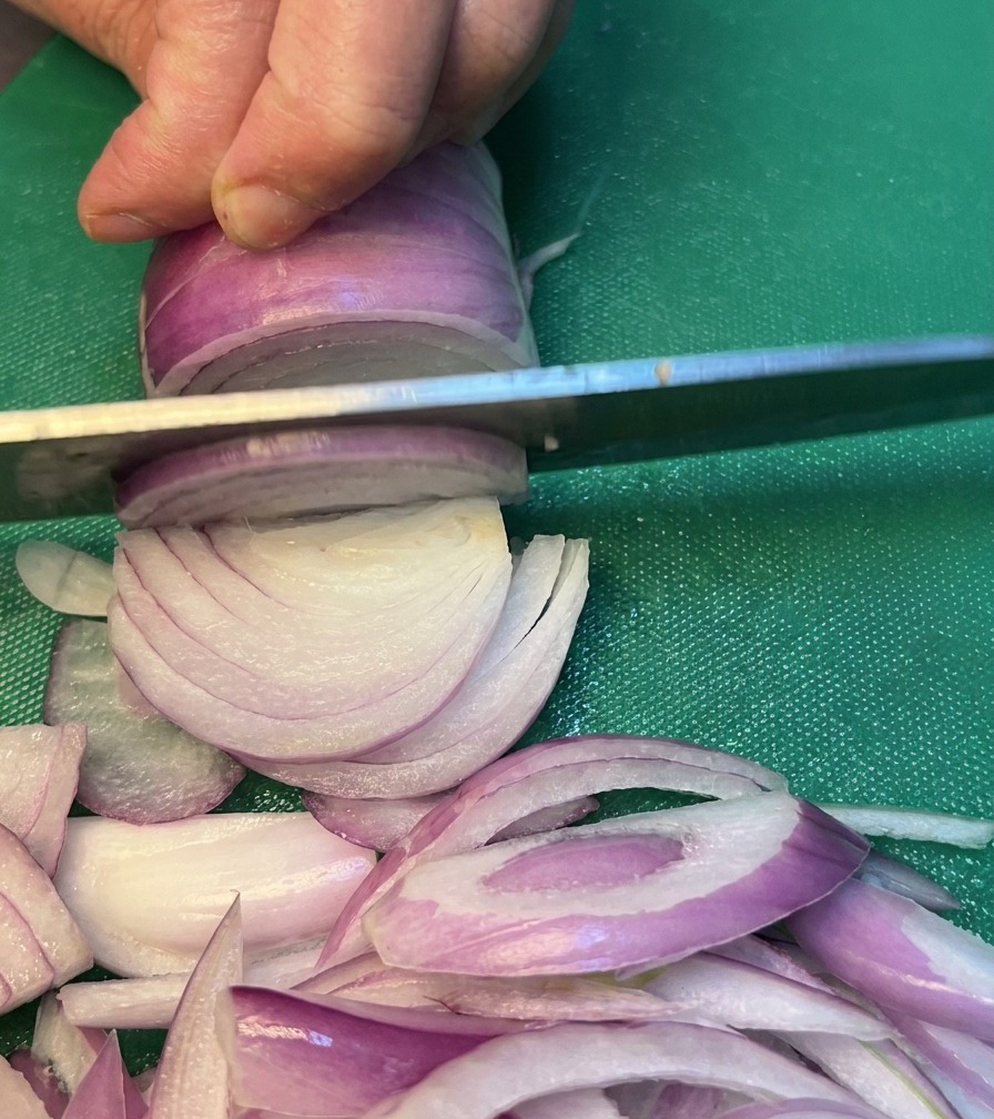 Onions being carefully sliced on a green cutting board.