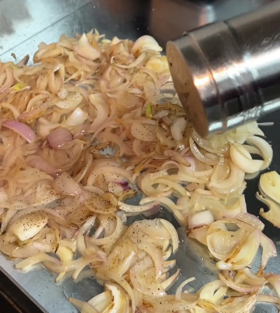 Salt and black pepper being sprinkled onto sautéed onions in the pan.