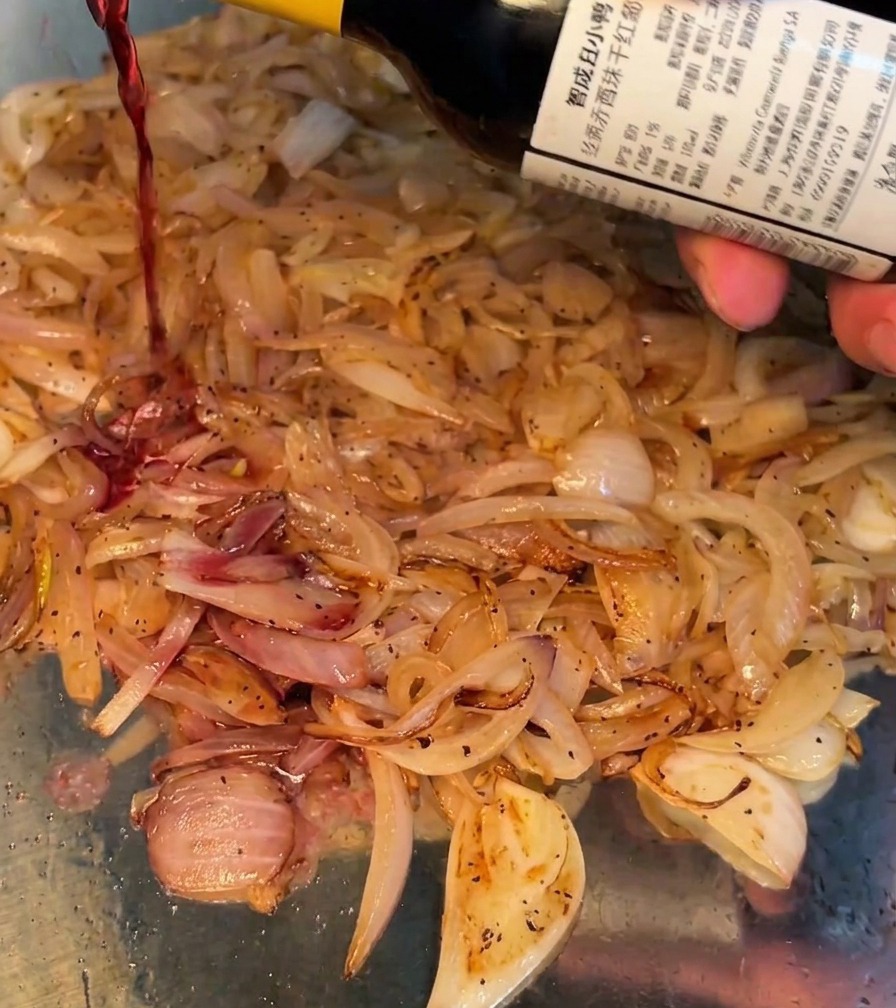 Red wine being poured into the pan of sautéing onions.