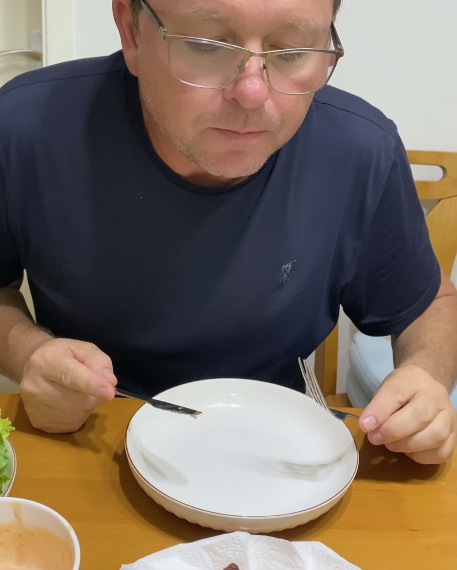 A person assembling a burger on a plate, adding caramelized onions and fresh vegetables to a beef patty on a bun.