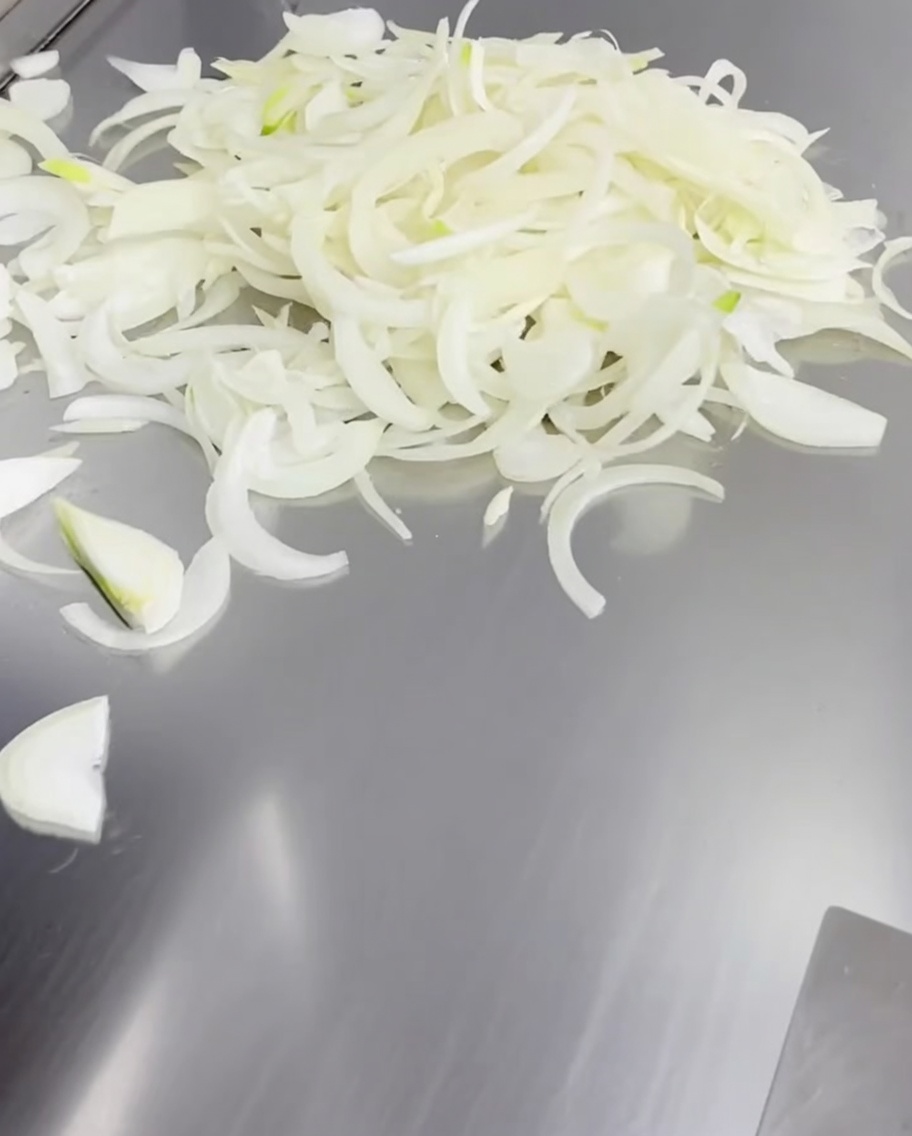 Thinly sliced white onions spread across a hot metal griddle surface.