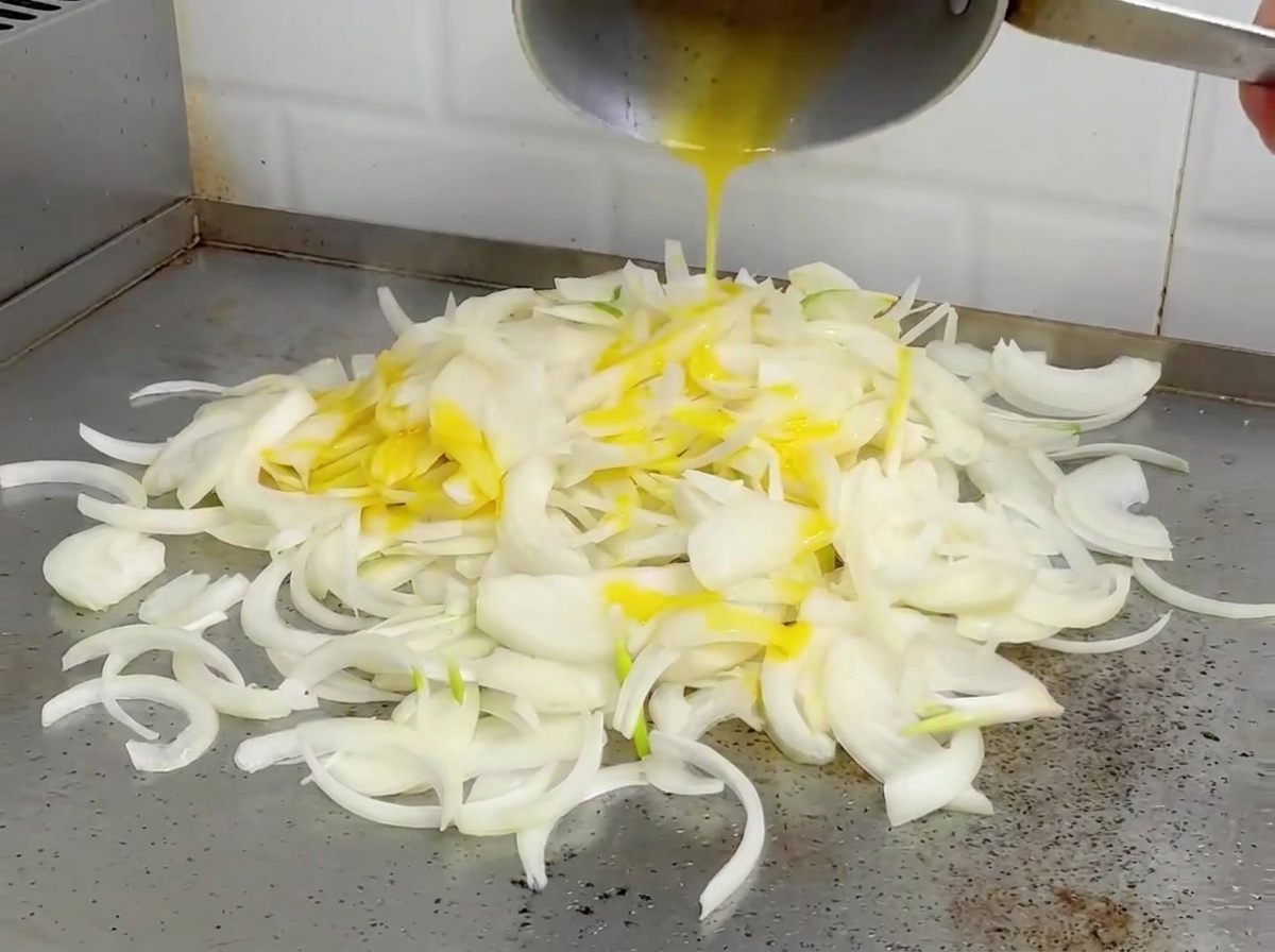 Onions being tossed and stir-fried on a hot griddle, appearing softened and lightly browned.