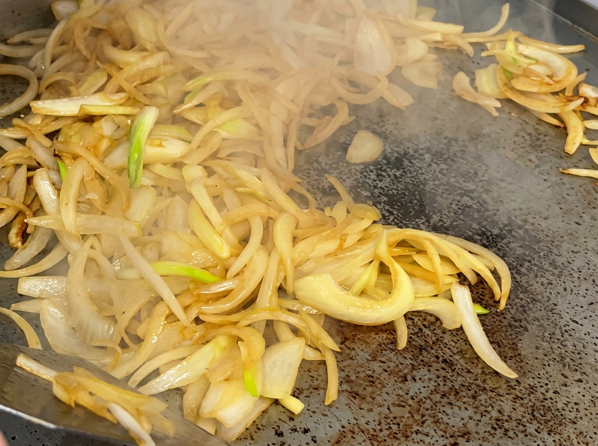 A stream of red wine being poured onto the cooking onions on a hot griddle.