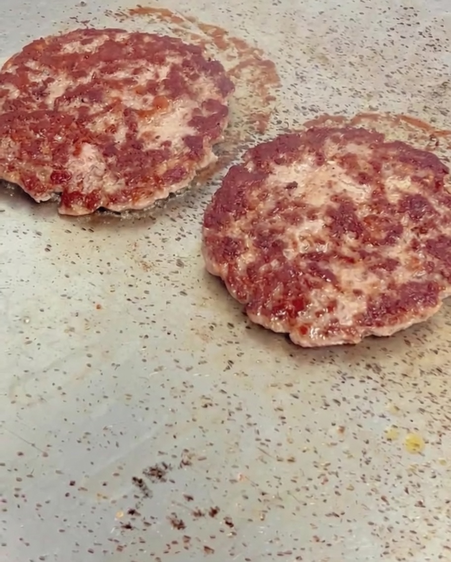 Slices of yellow cheese melting on top of hot, browned beef patties on a griddle.