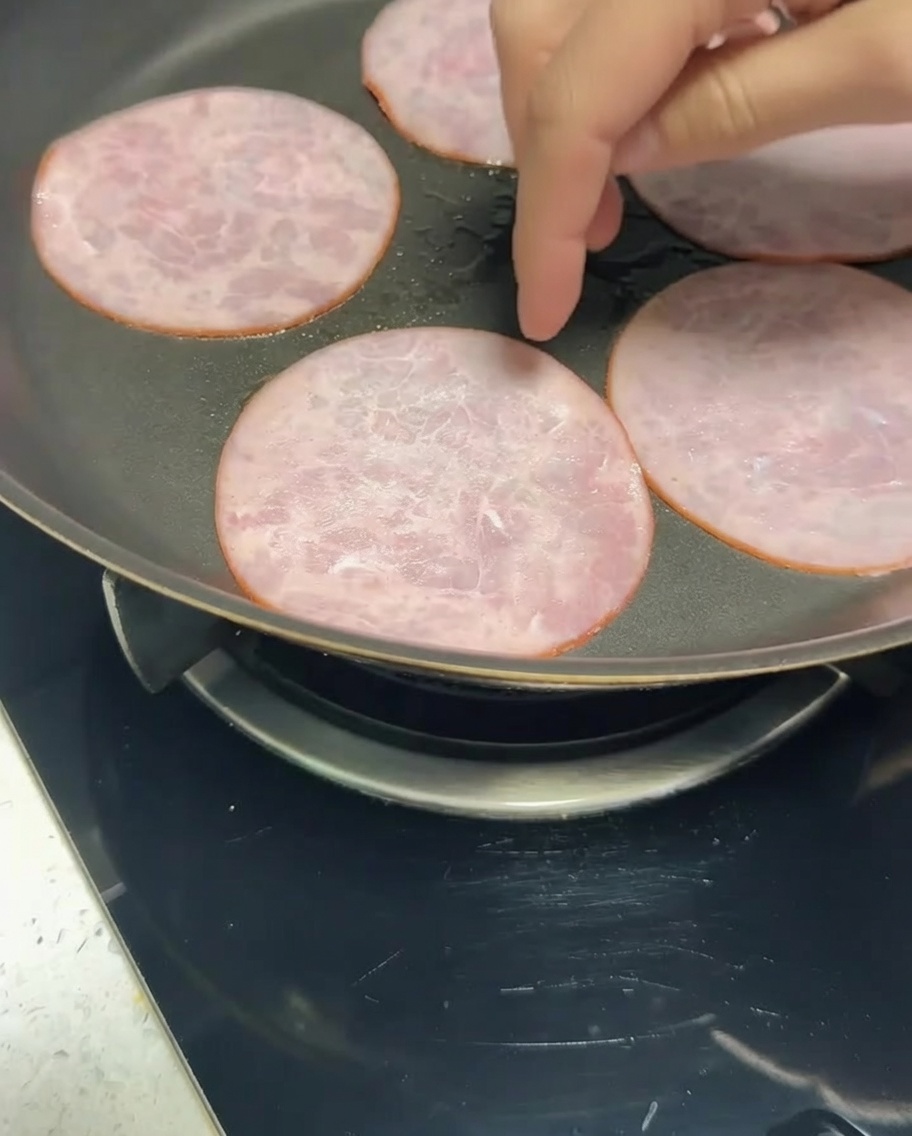 Slices of reduced-fat bacon frying in a pan until browned.