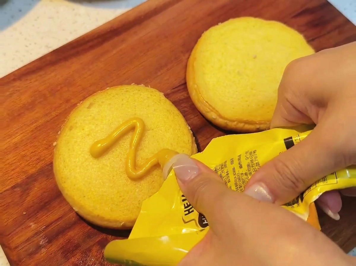 Honey mustard being spread on a toasted bun.