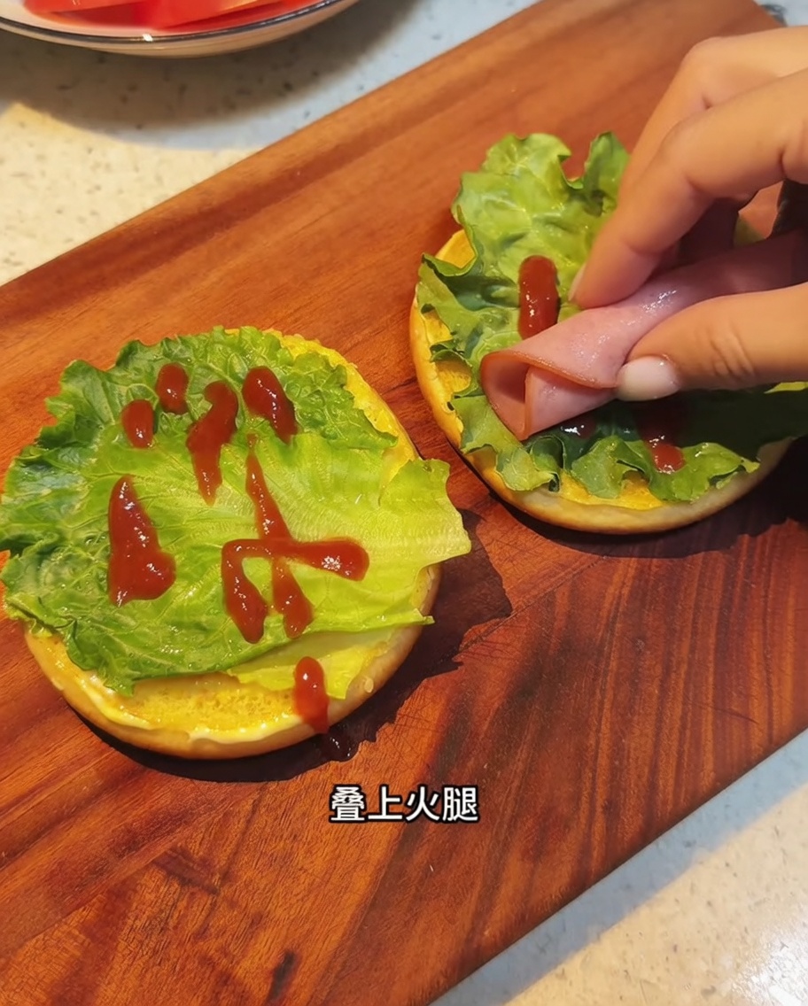 Crispy fried bacon slices being arranged on top of the lettuce and sauce layers on a hamburger bun.