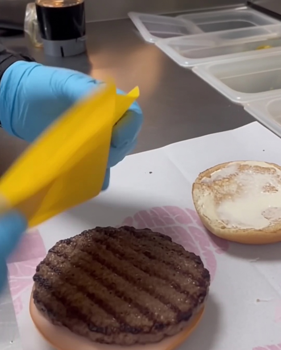 Close-up of a slice of yellow cheddar cheese resting on top of a grilled beef patty.