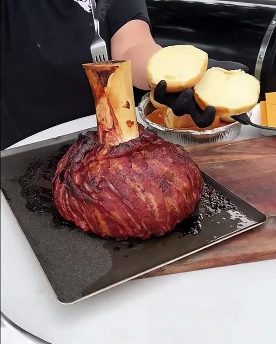 A spoonful of rich, roasted bone marrow being spread onto the surface of a toasted, golden-brown burger bun.