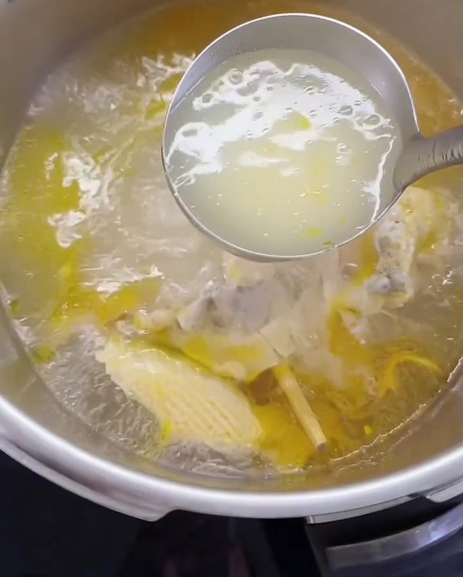 A ladle transferring chicken broth and shredded meat into a cooking pot.