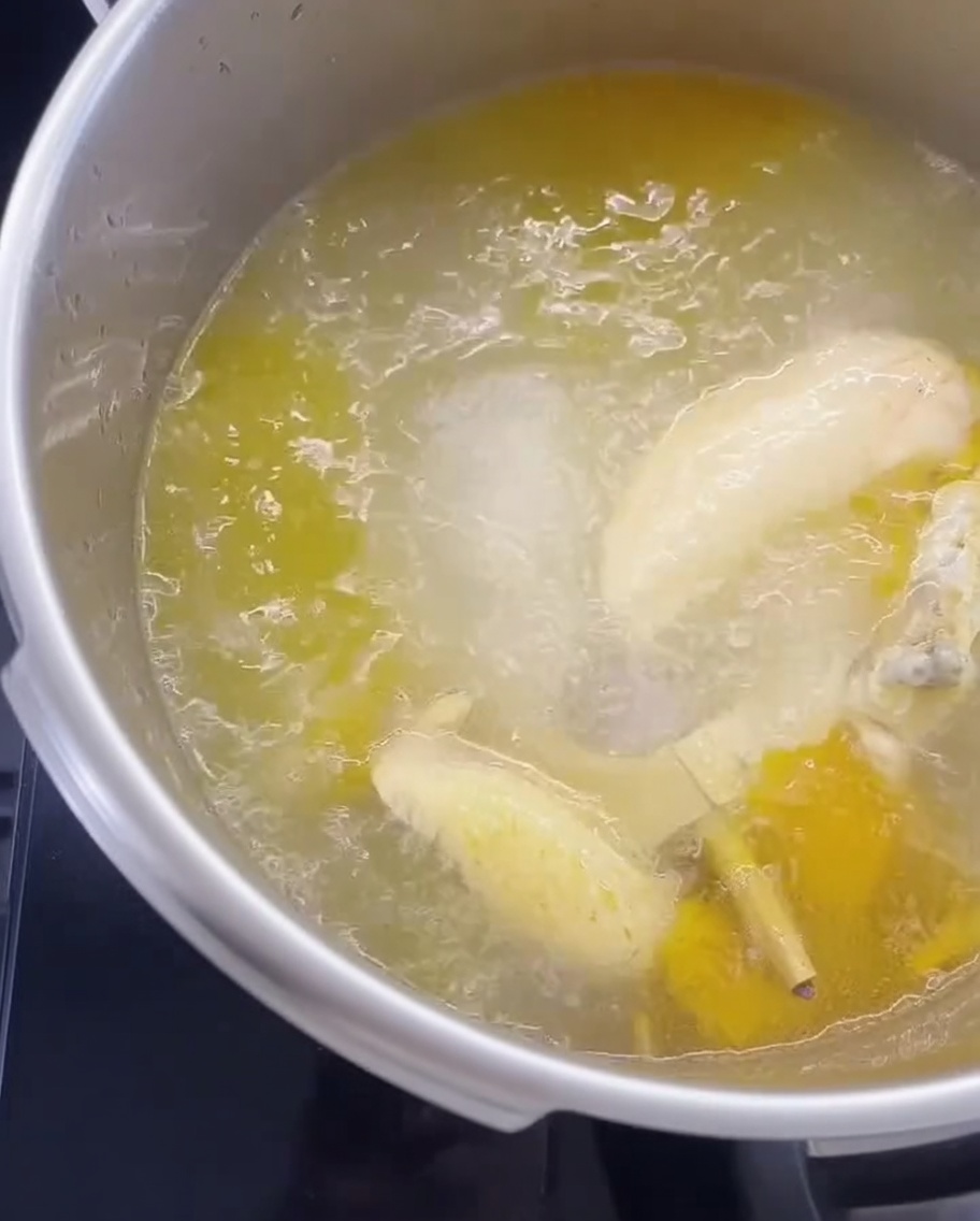 Dry noodles submerged in a pot of boiling chicken broth.
