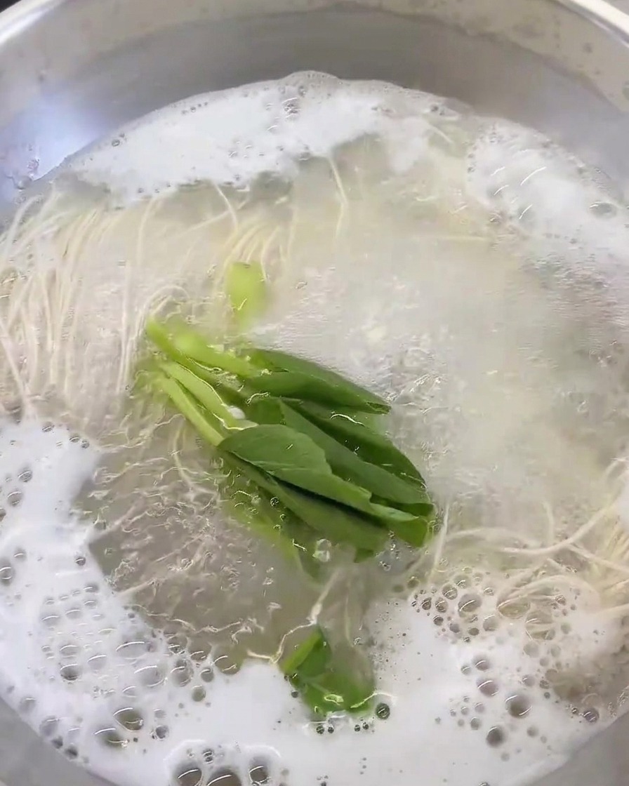 Fresh leafy green vegetables added to the pot of boiling broth and noodles.
