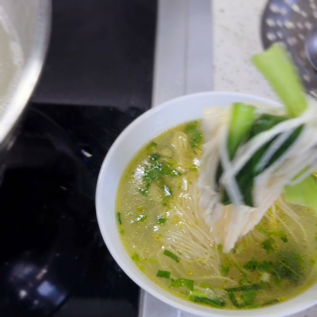 A bowl filled with hot noodles, green vegetables, and tender shredded chicken ready to be served.