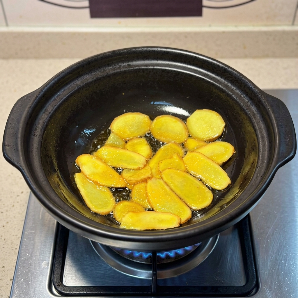 Golden-brown ginger slices frying in shimmering sesame oil inside a clay pot.