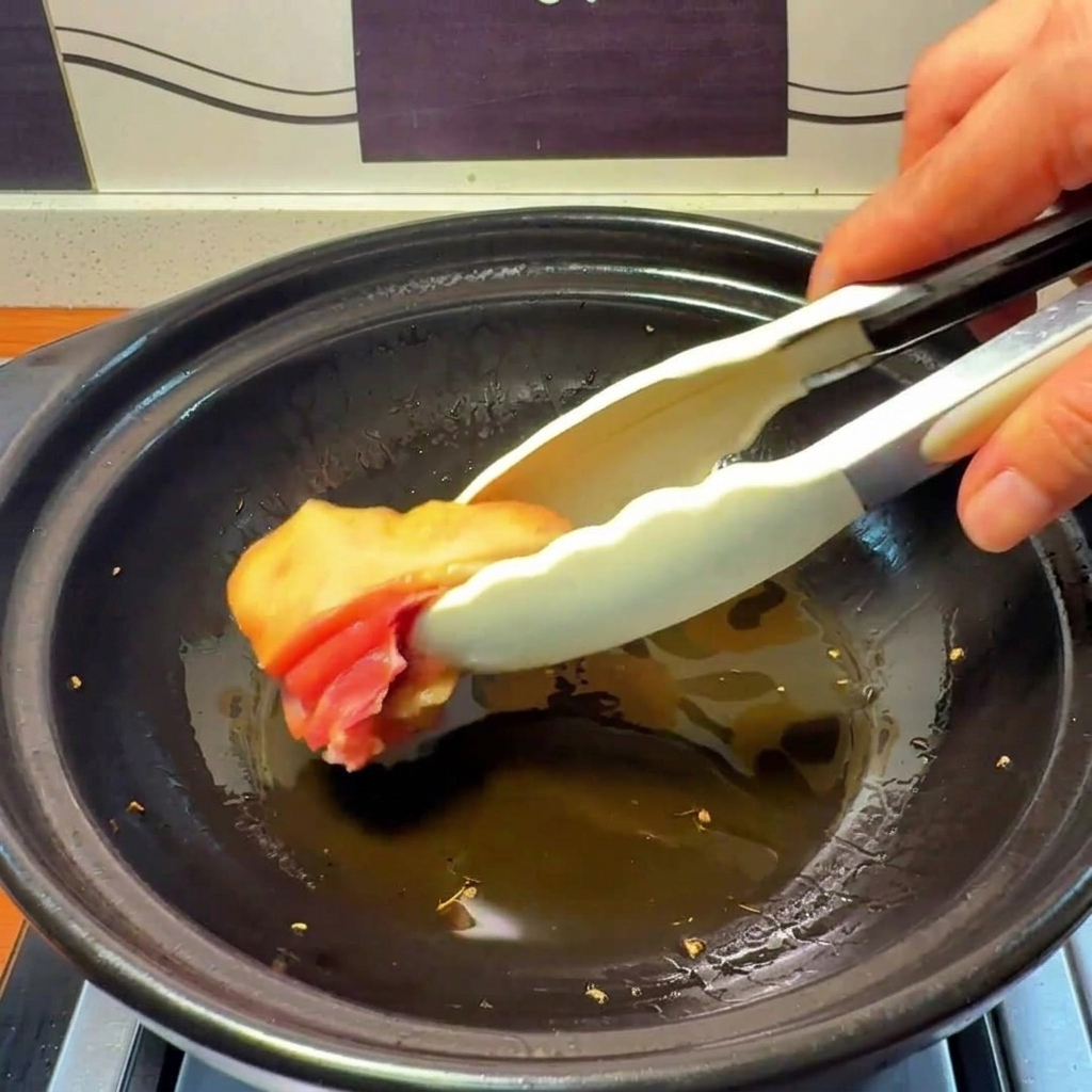 Pieces of raw chicken being placed into a clay pot with hot, ginger-infused oil.