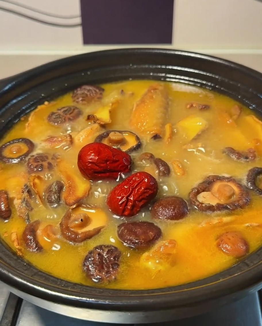 Red dates floating in the bubbling chicken and mushroom broth inside a clay pot.