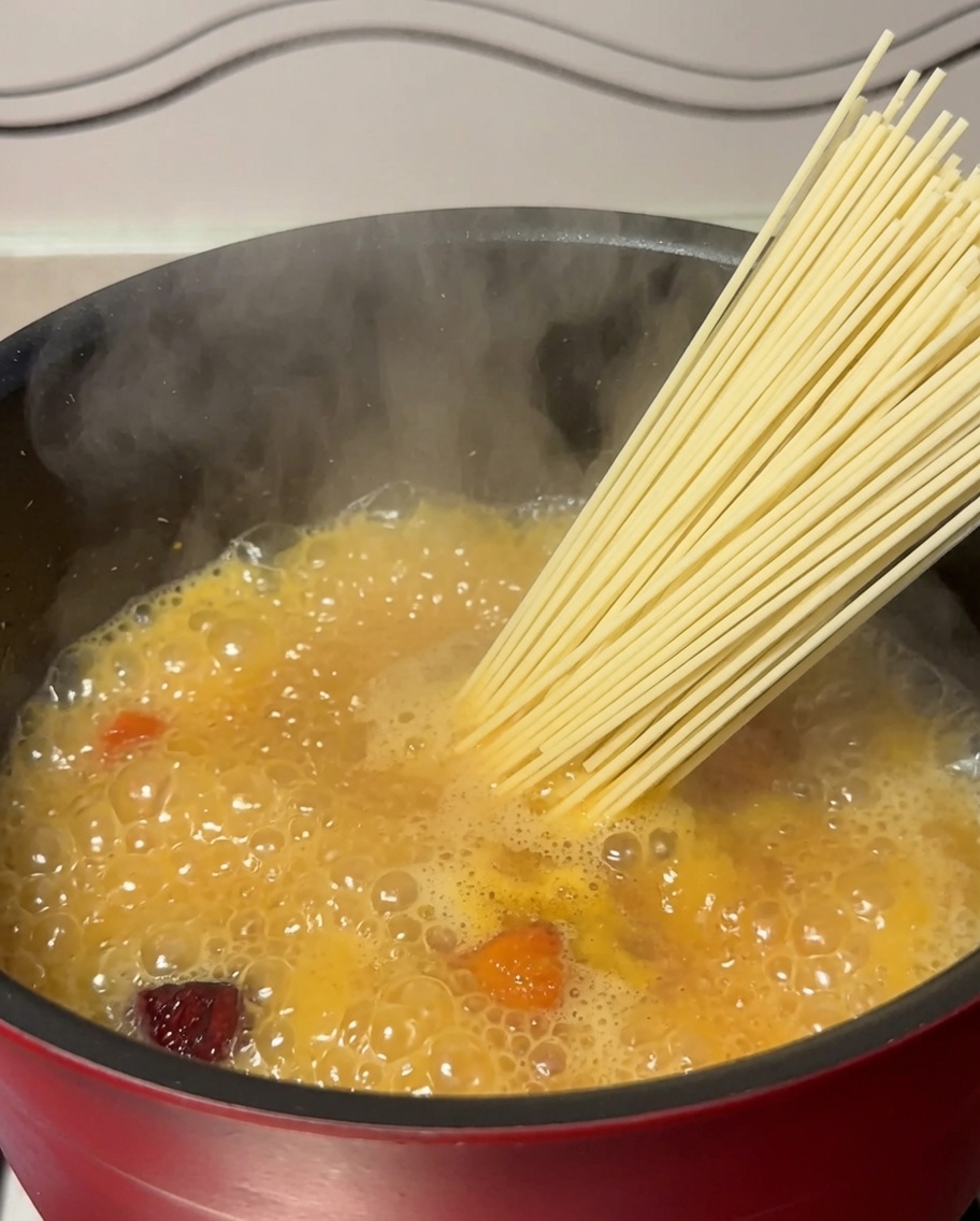 Dried noodles being placed into a pot of boiling chicken soup.
