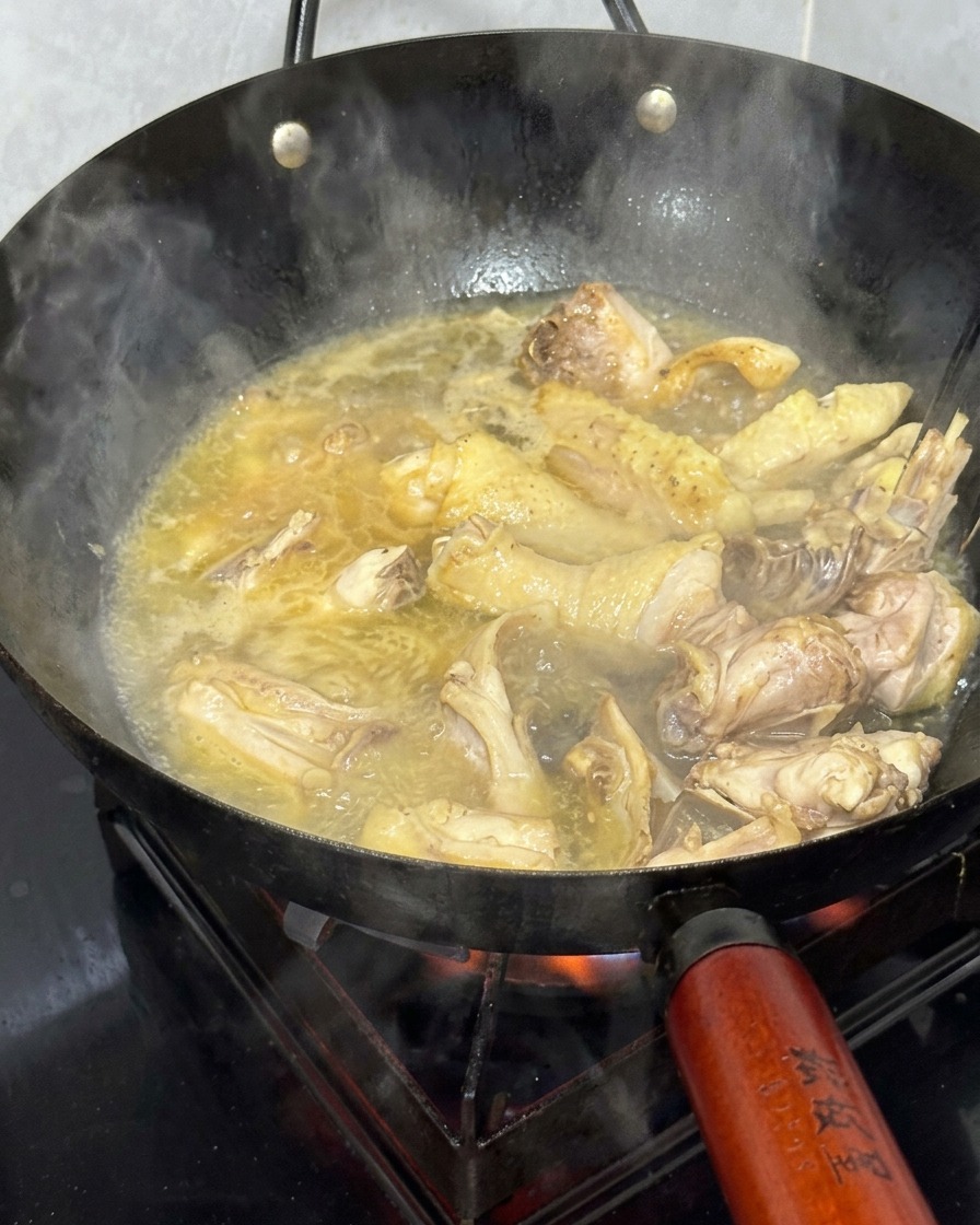 Chicken pieces simmering in a wok filled with a golden, bubbling hot broth.