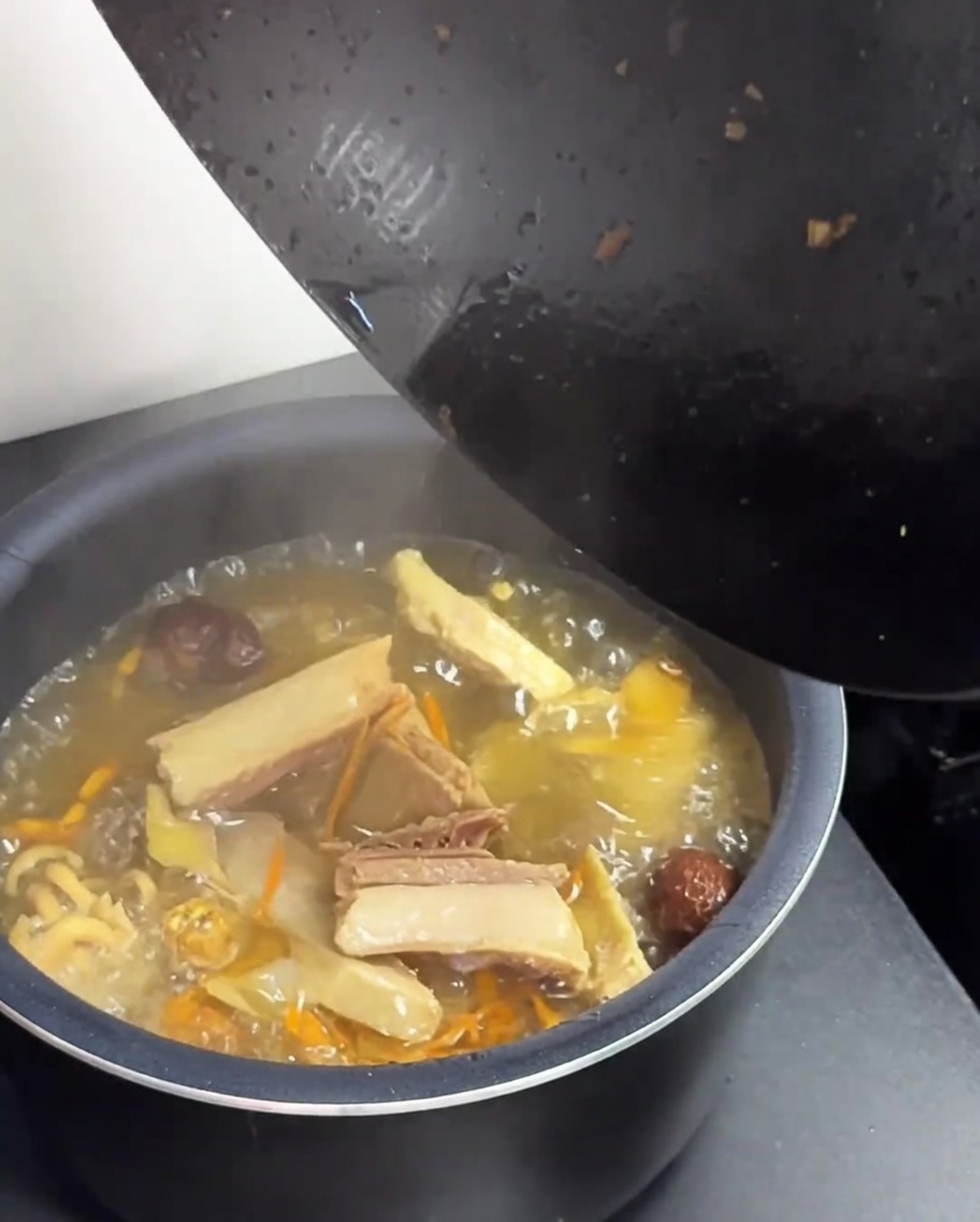 Transferring the hot chicken and mushroom soup from a black wok into a green rice cooker pot.