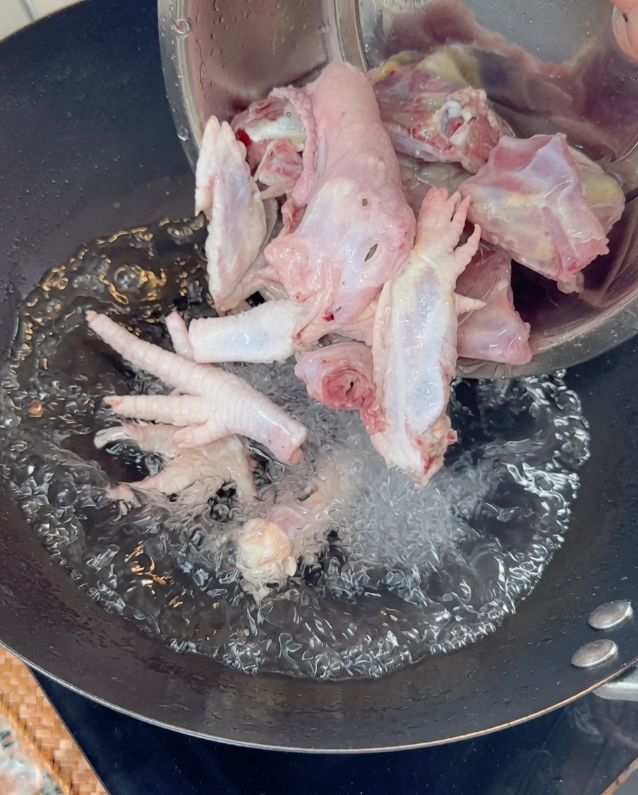 Pouring raw chicken bones and feet into a wok of boiling water.