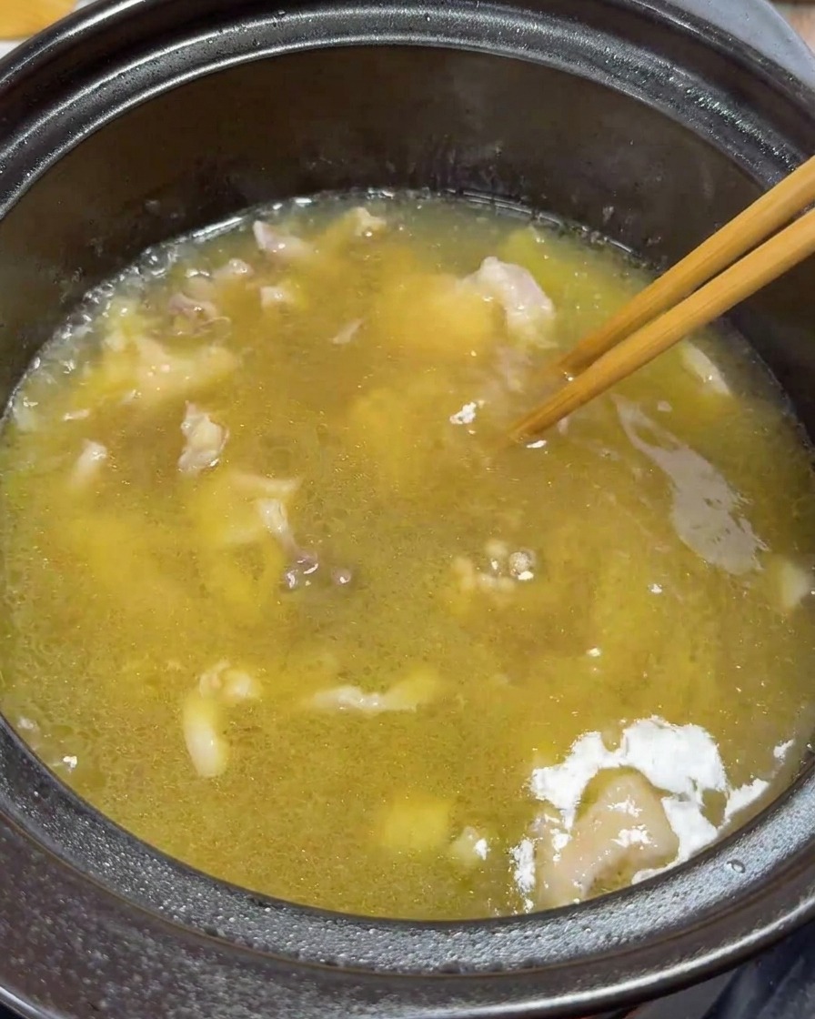 Chopsticks gently stirring chicken slices and yolks in the simmering soup.