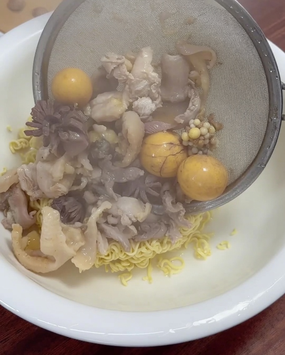 Freshly cooked chicken meat and yellow yolks being strained and placed into a bowl of noodles.
