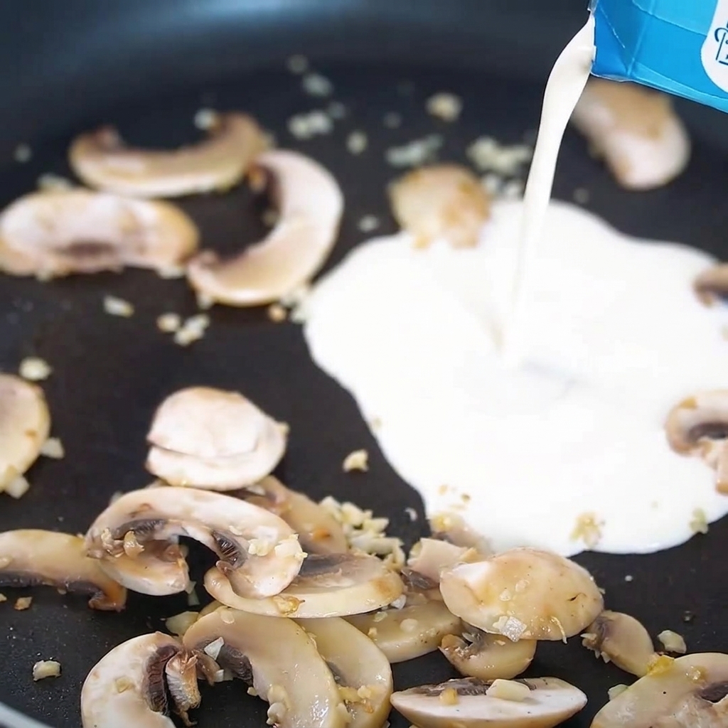 Cream being poured into a pan filled with cooked mushrooms and garlic.