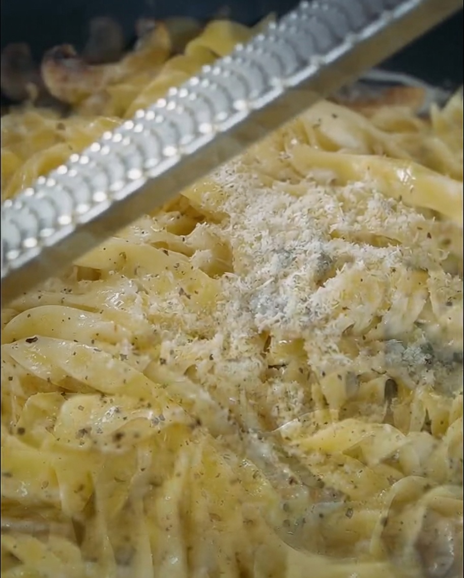 Hard cheese being freshly grated over a pan of creamy truffle pasta.