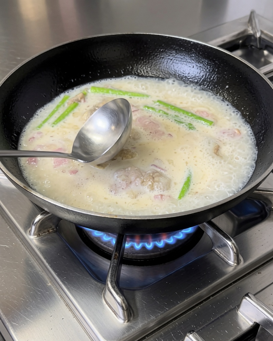 Cooked penne pasta being mixed into the creamy bacon and vegetable sauce in a frying pan.