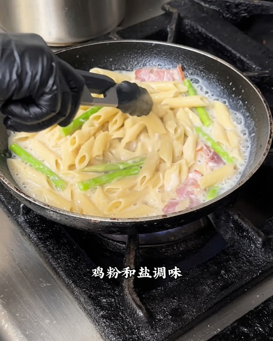 Penne pasta being stirred with white sauce and black truffle in a frying pan over medium heat.