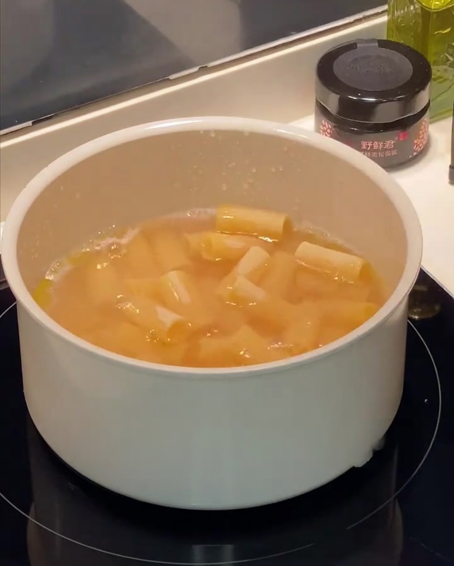 Rigatoni pasta boiling in a pot of water with visible bubbles and oil droplets on the surface.
