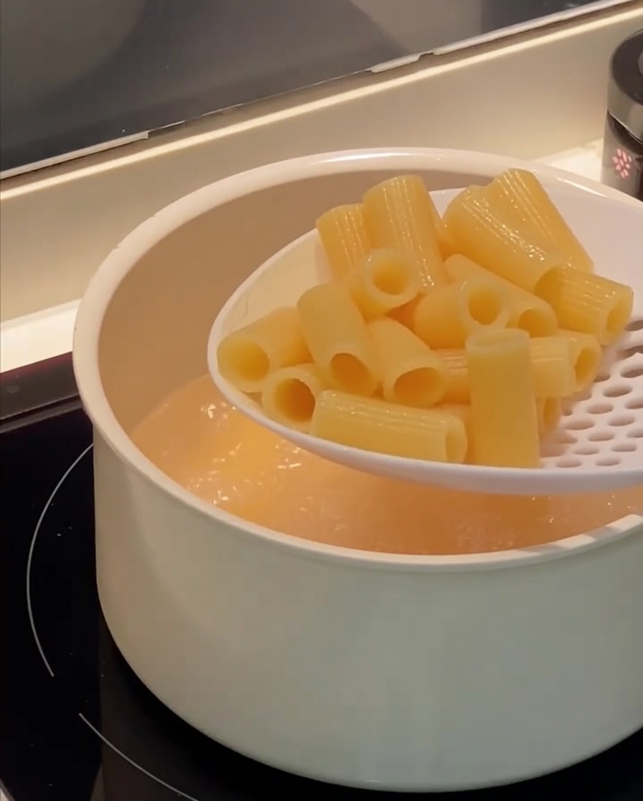 A slotted spoon lifting cooked rigatoni pasta out of a pot of boiling water.