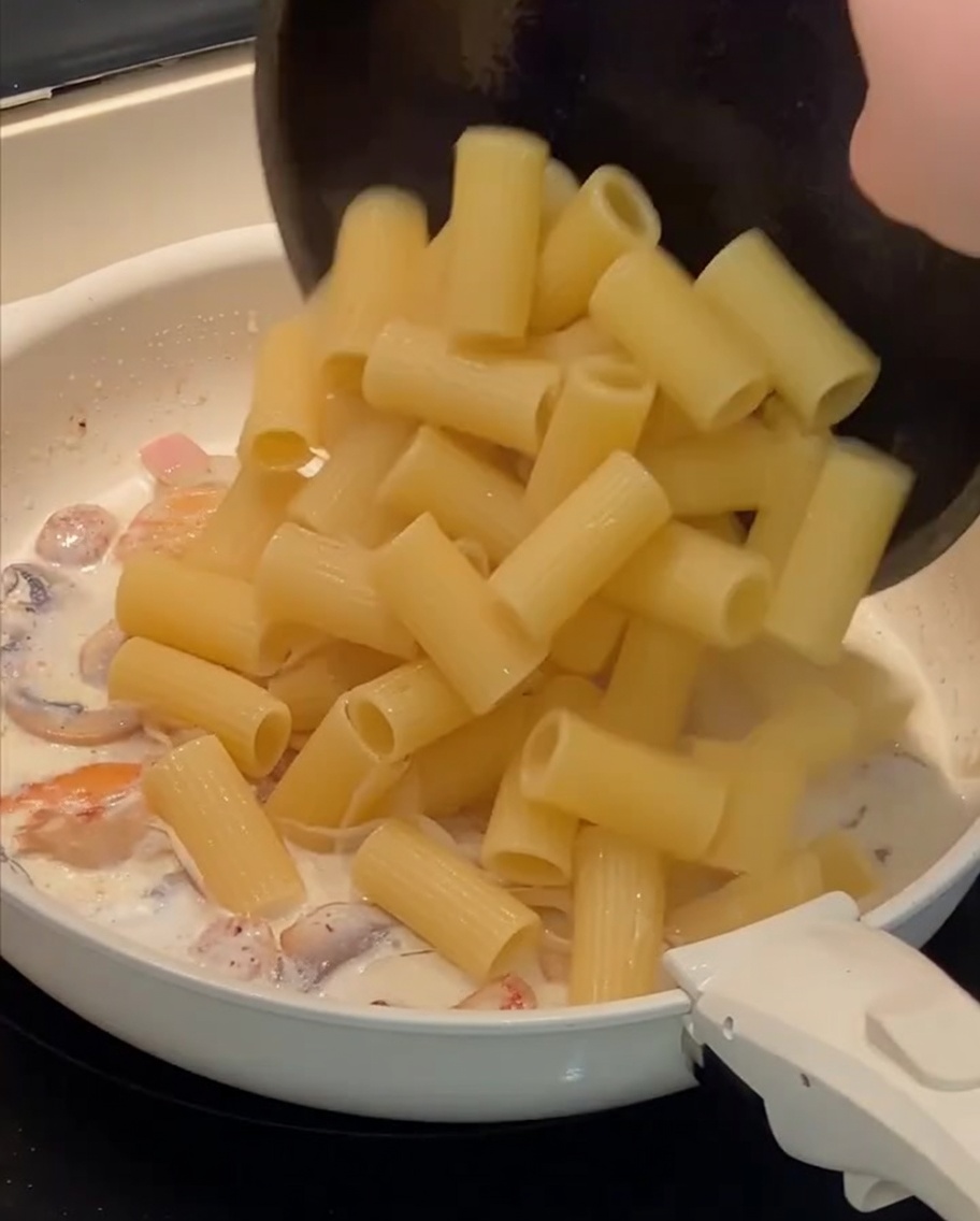 Cooked rigatoni pasta being added to the pan containing the creamy sauce and other ingredients.