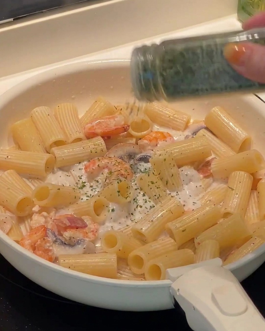 Freshly chopped parsley being sprinkled over the finished rigatoni pasta in the pan.