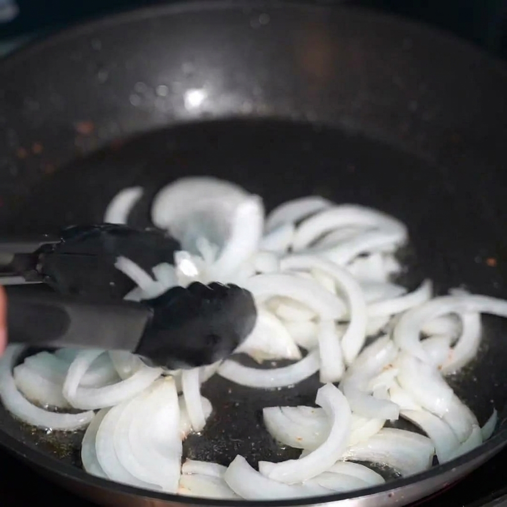 Translucent sliced onions stir-frying in clear golden bacon oil.