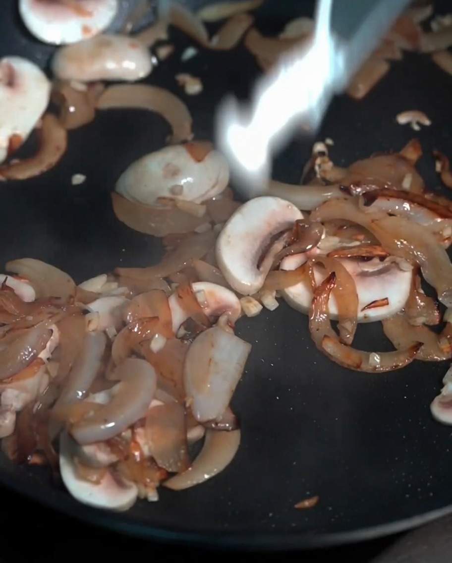 A variety of fresh mushrooms including button and beech varieties sautéing in a pan.