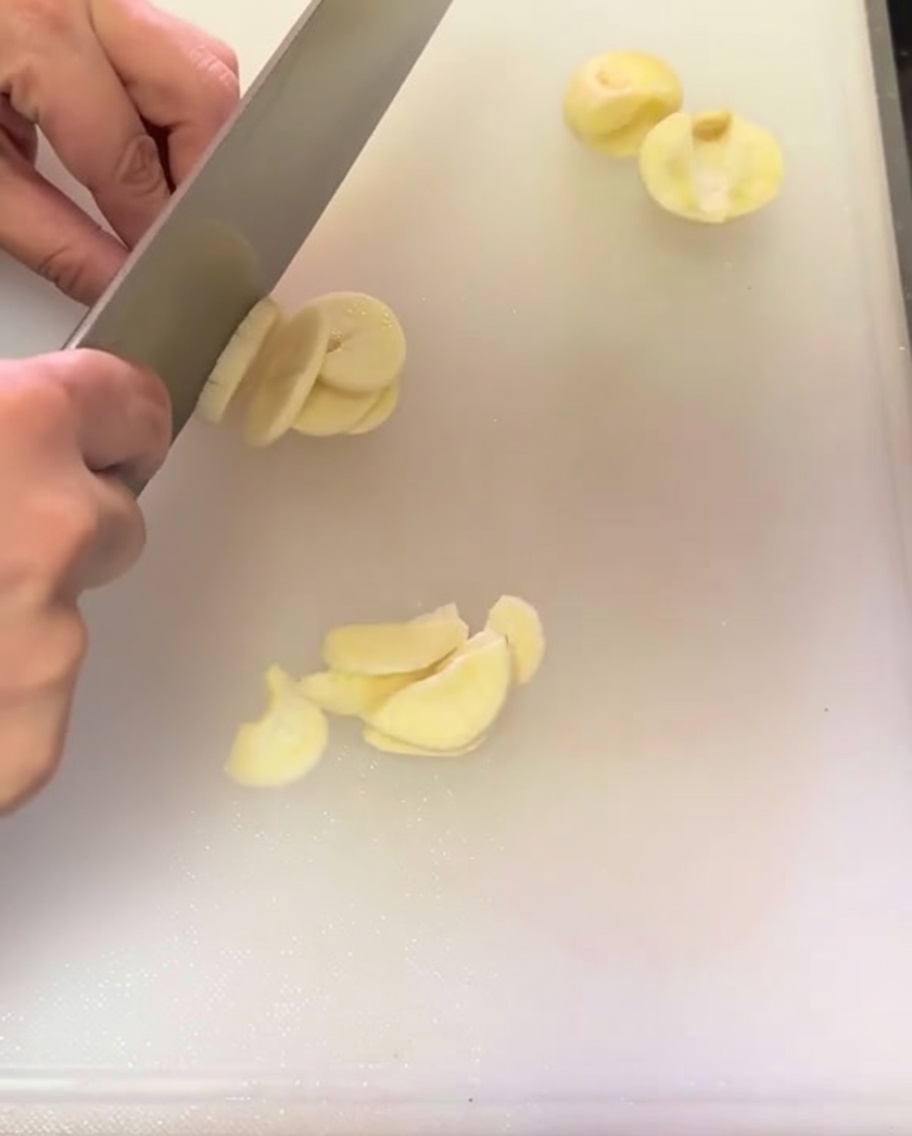 Thinly sliced garlic cloves spread across a white cutting board.