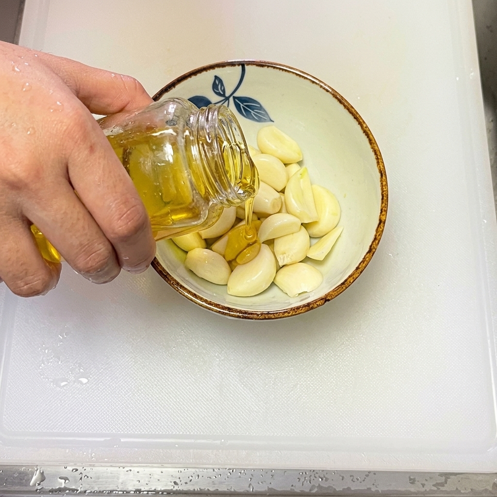 Olive oil being poured into a bowl containing fresh, thinly sliced garlic.