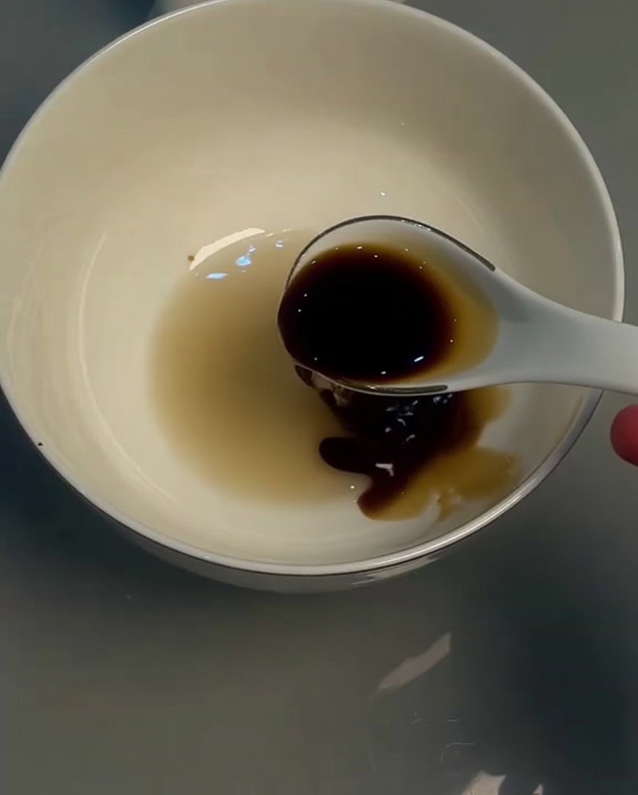 Light soy sauce in a white bowl being stirred with a spoon.