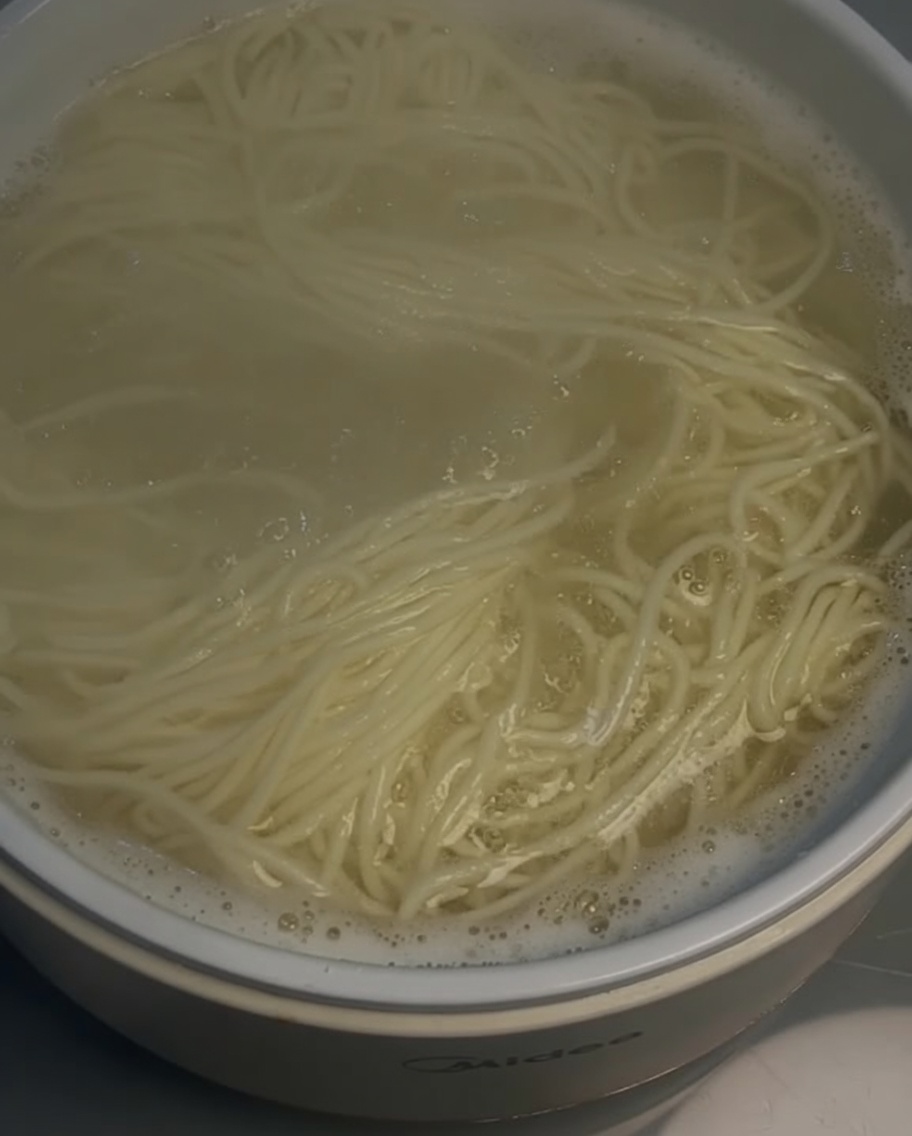 Strainer lifting cooked noodles from a pot.
