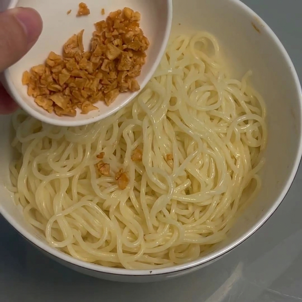 Crispy fried garlic being sprinkled onto the bowl of noodles.