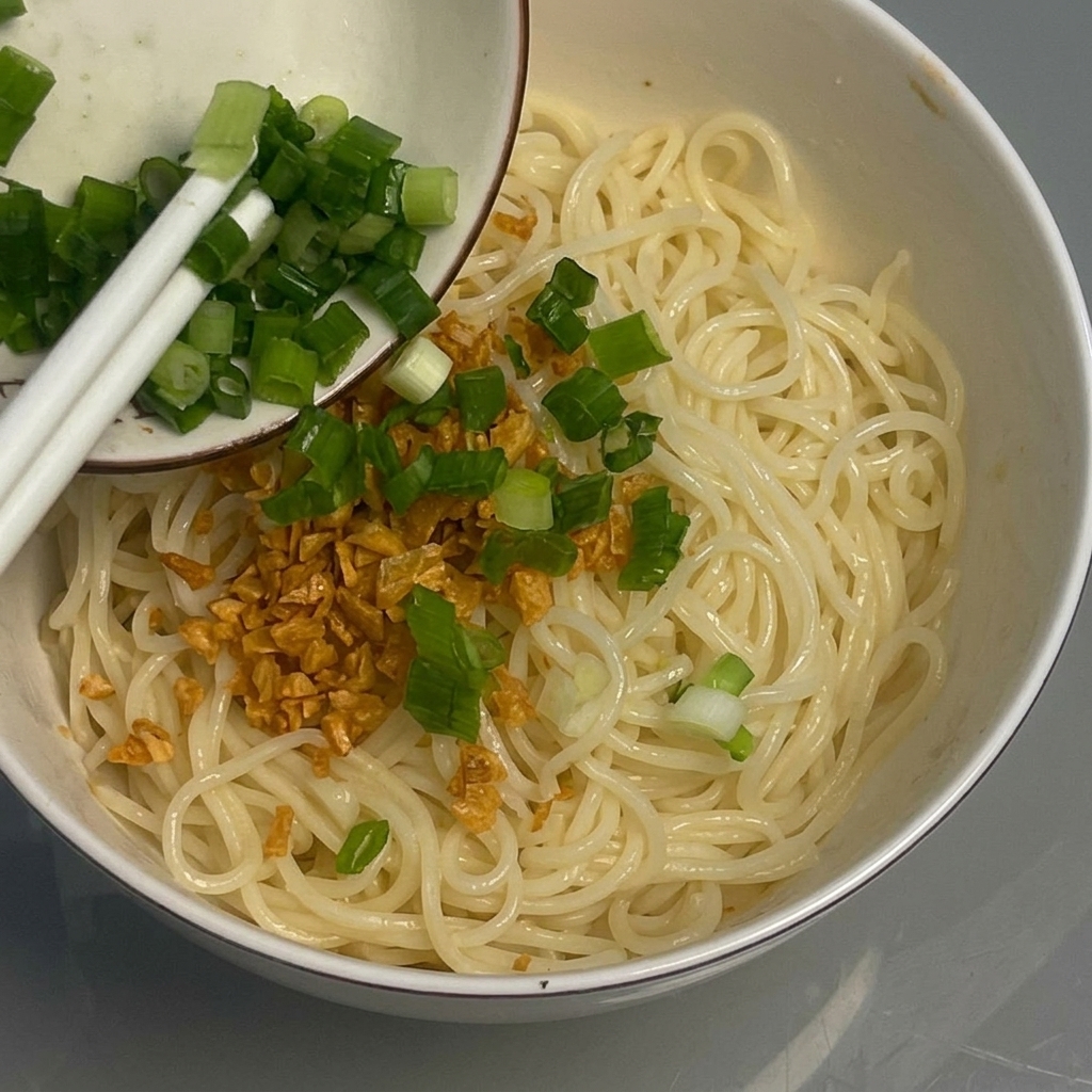Chopped green onions being added as a garnish to the noodles.